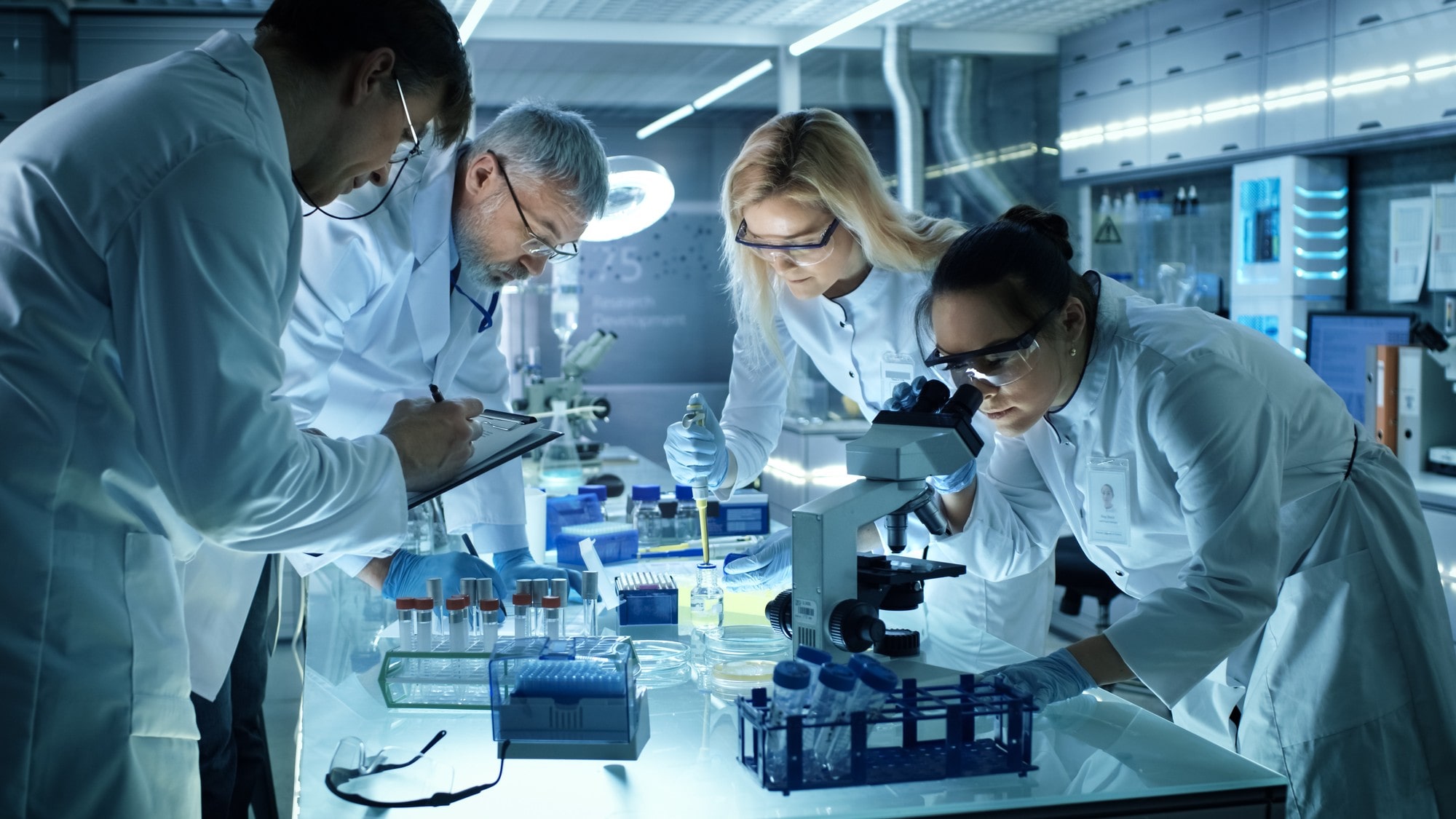 A Group Of People In Lab Coats Looking at A Microscope